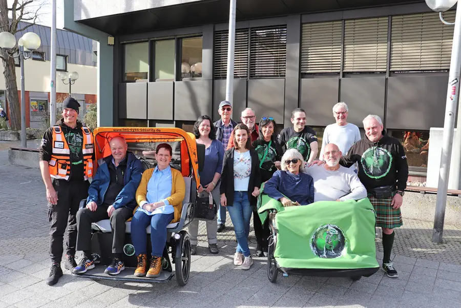 2 E-Rikschas mit Passagieren, dahinter das Team. 