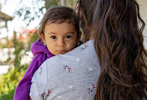 Rücken einer Frau mit langen dunklen Haaren, die ein Kind trägt 