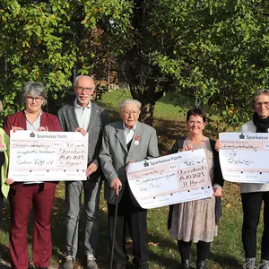 Vier Frauen und zwei Männer halten drei große symbolische Schecks in die Kamera