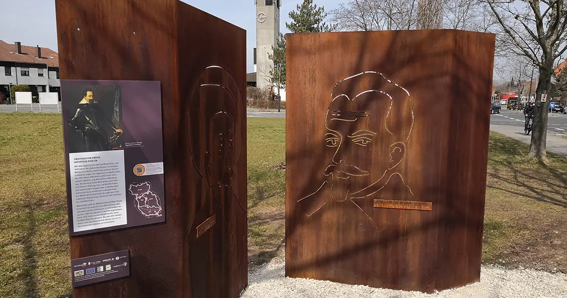 Die zwei Stelen aus Corten-Stahl mit der Festwiese und dem Kirchturm von St. Markus im Hintergrund zeigen die großen Bildnisse von König Gustaf Adolf von Schweden und Albrecht von Wallenstein