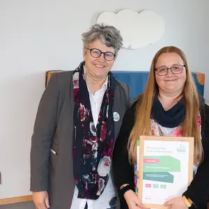 Zwei Frauen, eine hält eine Urkunde.