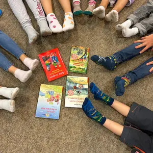 Vier Bücher in der Mitte des Bildes und darum herum die Beine und Füße der Teilnehmer:innen.