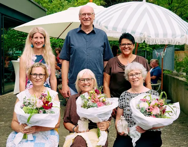 Drei Damen sitzend mit Blumenstrauß, dahinter ein Mann und zwei Frauen