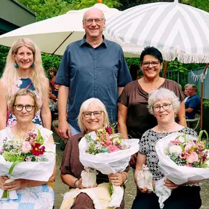 Drei Damen sitzend mit Blumenstrauß, dahinter ein Mann und zwei Frauen