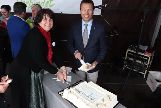 Eine Frau und ein Mann schneiden eine große rechteckige Torte mit dem Logo "25 Jahre Stadt Oberasbach" an.