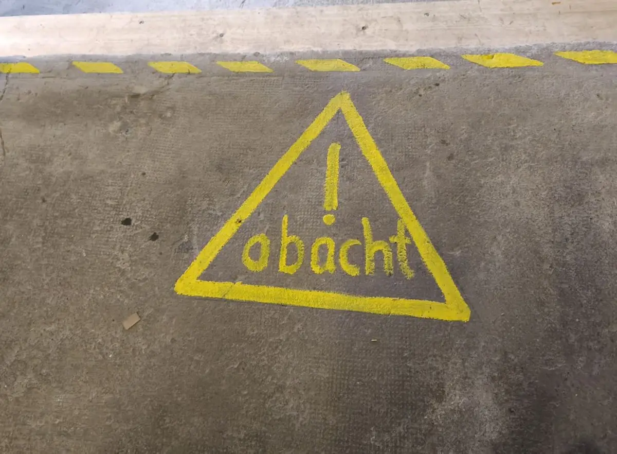 Ein gelbes Warndreick mit der Inschrift "Obacht" auf einem Betonboden