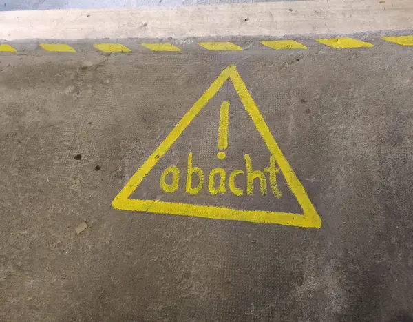 Ein gelbes Warndreick mit der Inschrift "Obacht" auf einem Betonboden