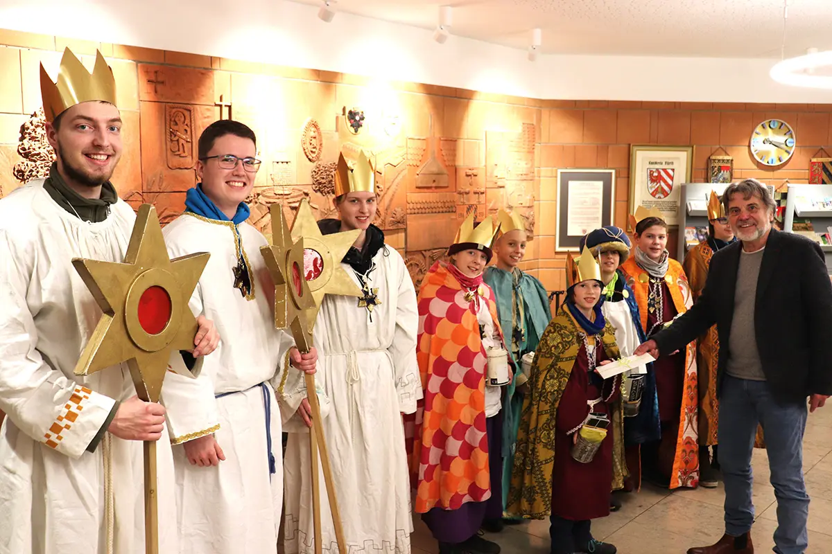 Sternsinger in ihren Gewändern im Rathausfoyer mit Bürgermeister Norbert Schikora, der einen Briefumschlag überreicht.