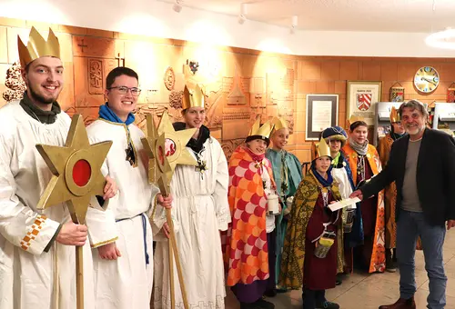 Sternsinger in ihren Gewändern im Rathausfoyer mit Bürgermeister Norbert Schikora, der einen Briefumschlag überreicht.