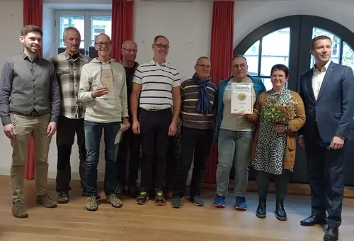 Eine Gruppe von Menschen hält einen Pokal und eine Urkunde in der Hand. 