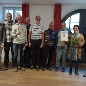 Eine Gruppe von Menschen hält einen Pokal und eine Urkunde in der Hand. 