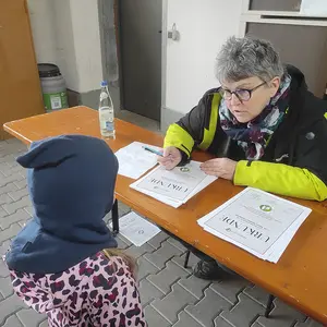 Eine Frau unterschreibt Urkunden auf einem Biertisch und unterhält sich mit einem Kind.