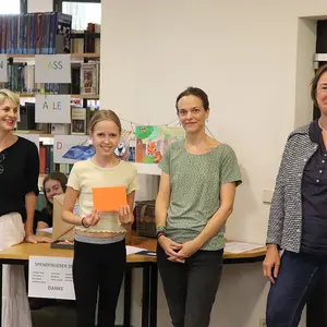 Ein Mädchen bei der Preisübergabe. Im Hintergrund drei Frauen vom Büchereiteam.
