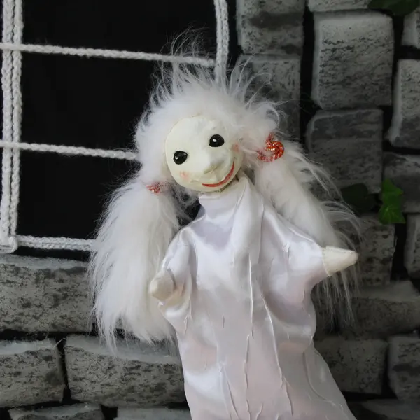 weiße Handpuppe mit langen Zöpfen vor der groben Steinwand eines Bühnenschlosses