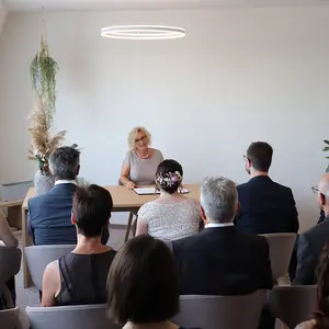 Die Hochzeitsgesellschaft hört der Standesbeamtin zu.