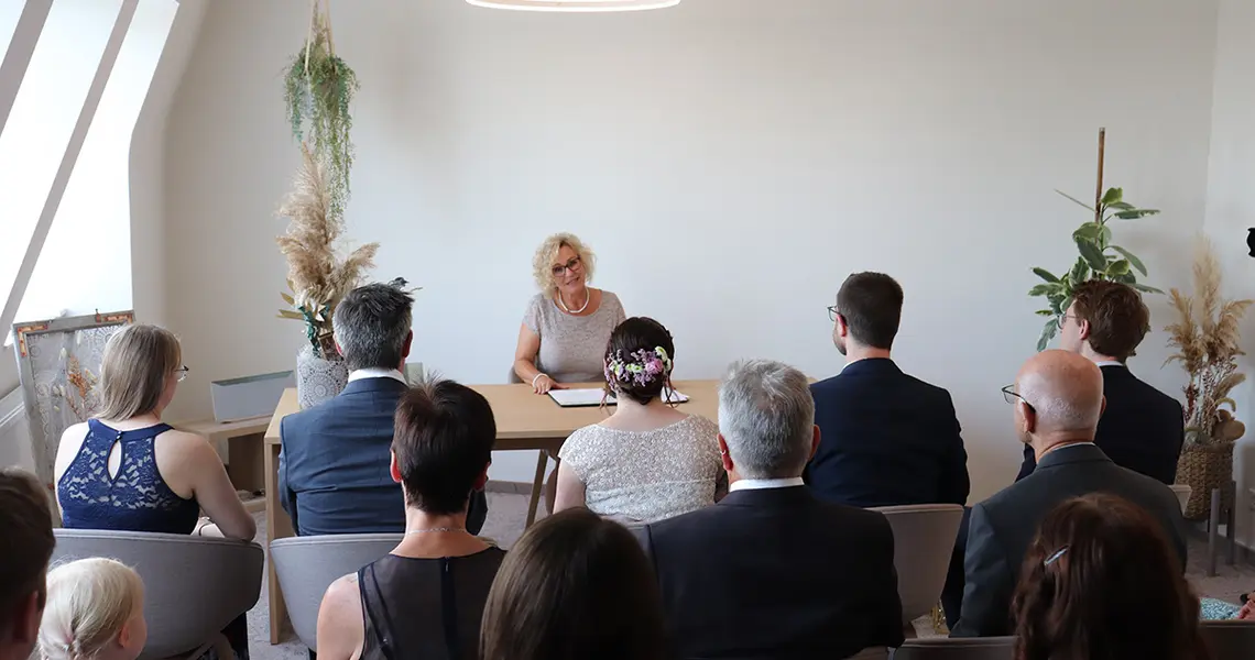 Die Hochzeitsgesellschaft hört der Standesbeamtin zu.