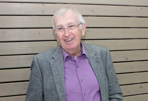 Portraitfoto eines älteren Herrn mit Brille vor einer mit Holz verkleideten Wand