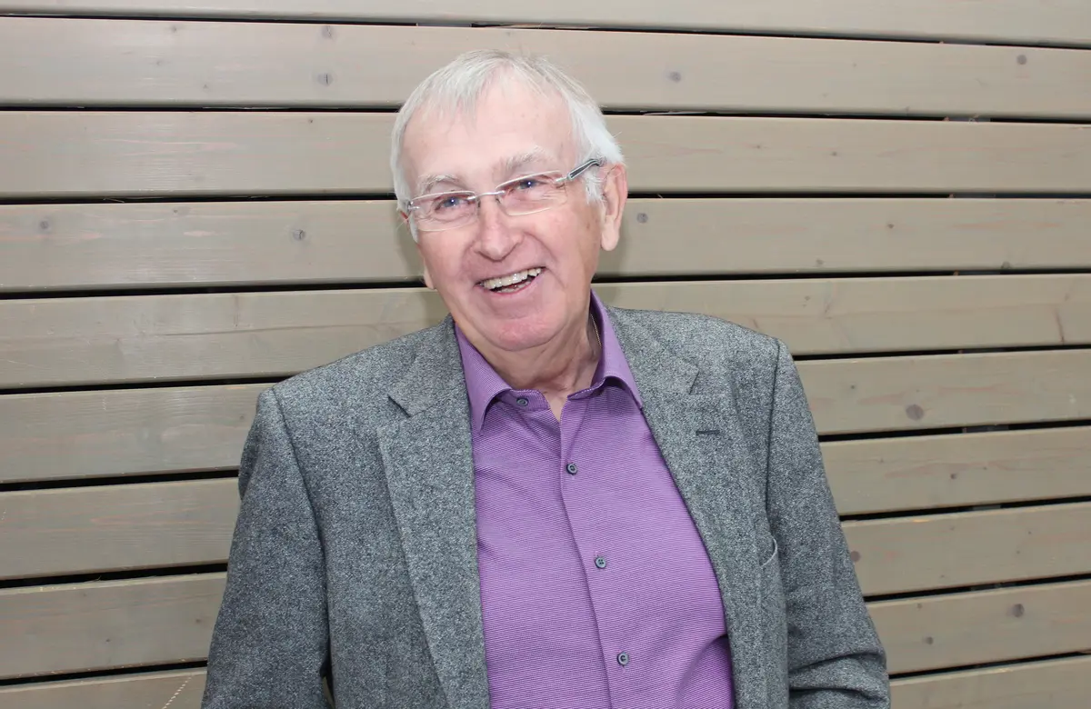 Portraitfoto eines älteren Herrn mit Brille vor einer mit Holz verkleideten Wand
