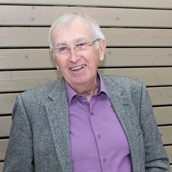 Portraitfoto eines älteren Herrn mit Brille vor einer mit Holz verkleideten Wand