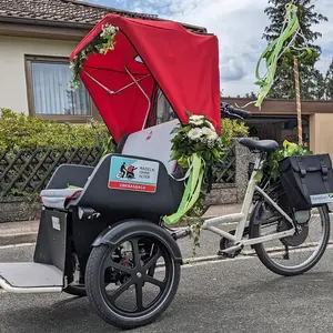 Die neue Elektro-Fahrrad-Rikscha der Stadt Oberasbach mit ihrem knallroten Dach, anlässlich ihrer Jungfernfahrt bei einem Kirchweih-Umzug festlich mit Blumen und einem Mini-Kärwabaum geschmückt