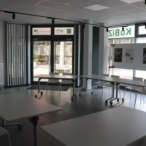 Blick in den Schulungsraum, leere Tische. Im Hintergrund Ausstellung in den Fenstern des Kubiz. 