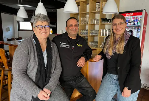 Zwei Frauen und ein Mann sitzen am Tresen eines Lokals.