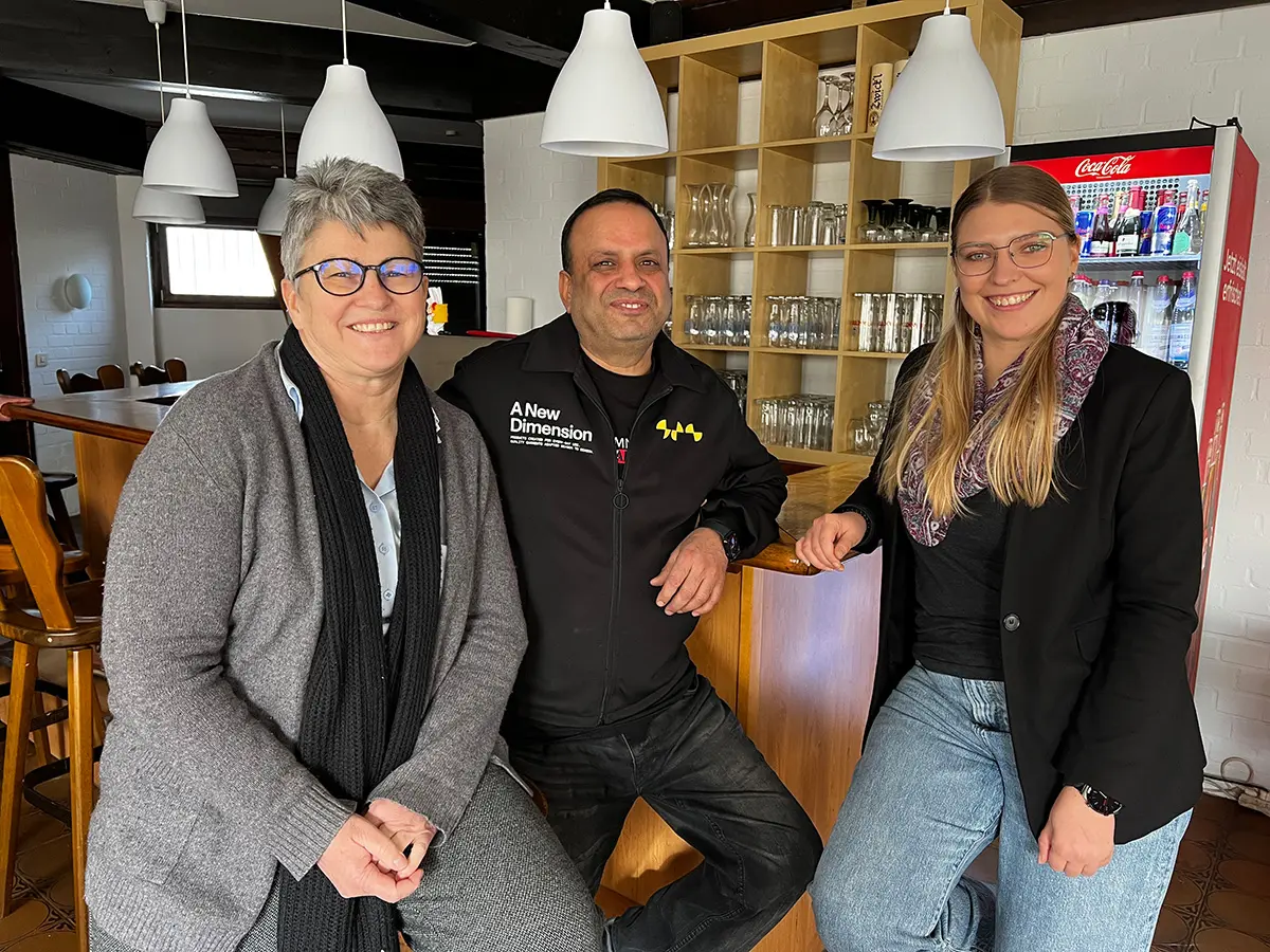 Zwei Frauen und ein Mann sitzen am Tresen eines Lokals.