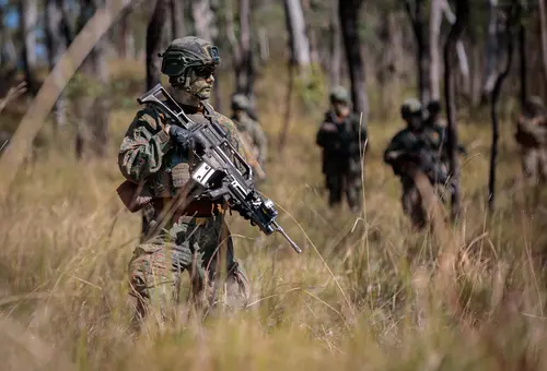 Soldat mit Gewehr im Wald, im Hintergrund weitere Soldaten 