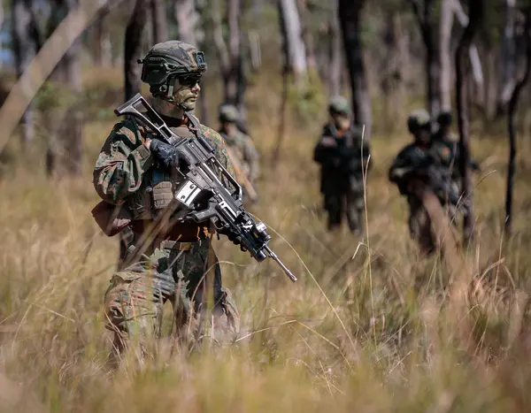Soldat mit Gewehr im Wald, im Hintergrund weitere Soldaten 