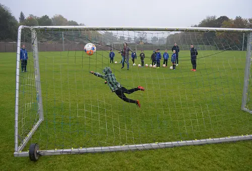 perspektive hinter dem Tor auf den Sportplatz: Torwart versucht, einen Ball zu fangen