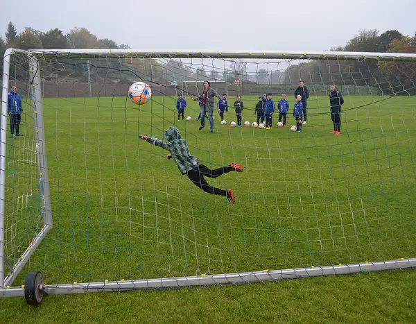 perspektive hinter dem Tor auf den Sportplatz: Torwart versucht, einen Ball zu fangen