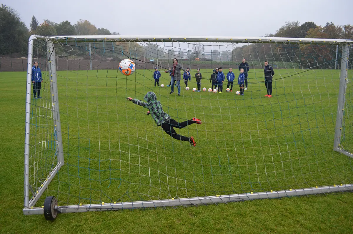 perspektive hinter dem Tor auf den Sportplatz: Torwart versucht, einen Ball zu fangen