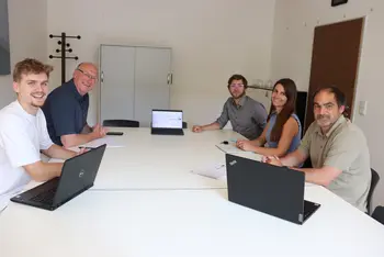 Vier Männer und eine Frau sitzen mit Laptops in einem Besprechungszimmer und schauen in die Kamera.