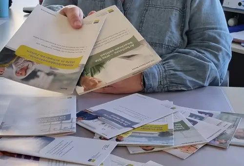 Mitarbeiterin reicht Broschüren über den Tisch 