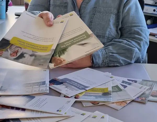 Mitarbeiterin reicht Broschüren über den Tisch 