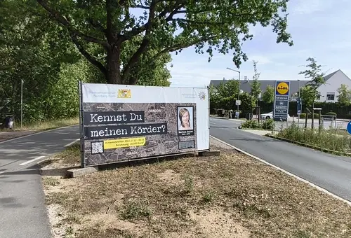 Seitenstreifen der Hainbergstraße mit dem Banner zum Cold Case. Darauf die Frage "Kennst du meinen Mörder?"