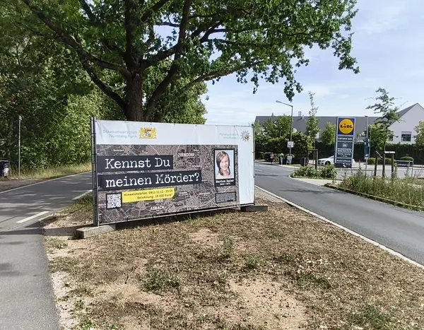 Seitenstreifen der Hainbergstraße mit dem Banner zum Cold Case. Darauf die Frage "Kennst du meinen Mörder?"