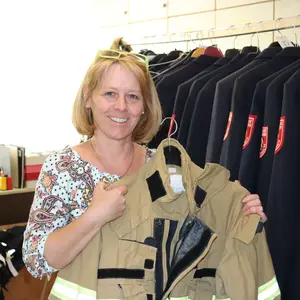 Claudia Weiß in der Kleiderkammer vor blauen Uniformen. In der Hand hält sie einen Einsatzanzug in braun.