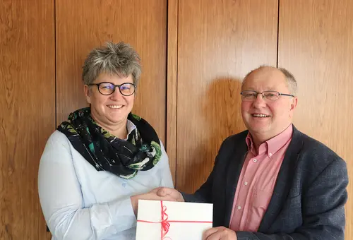Ein Mann und eine Frau stehen mit einem Geschenkgutschein vor einer Holzwand.