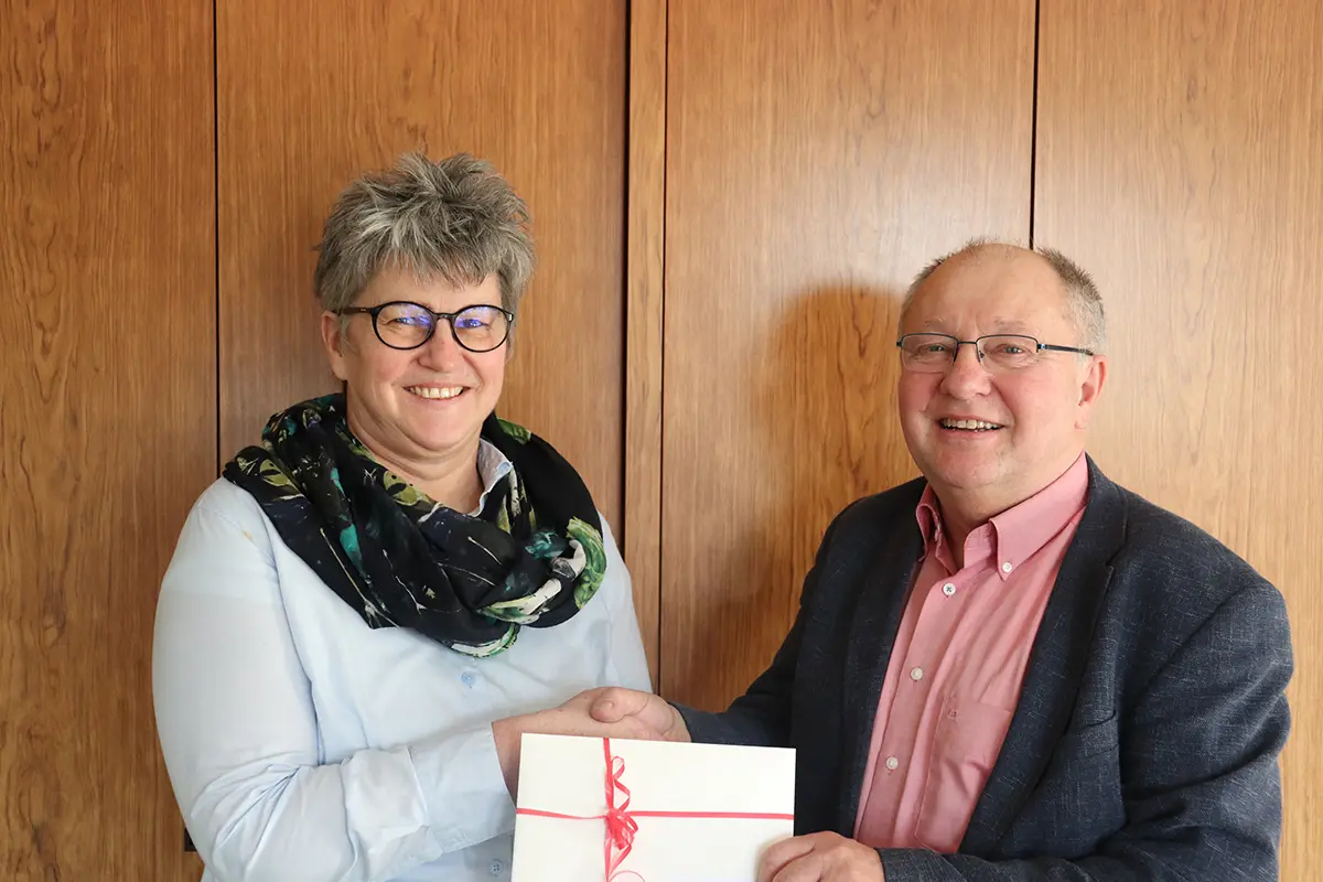 Ein Mann und eine Frau stehen mit einem Geschenkgutschein vor einer Holzwand.