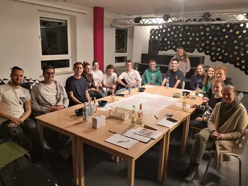 Um einen Tisch sitzen rund 16 Personen herum