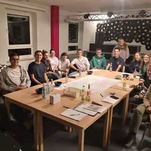 Um einen Tisch sitzen rund 16 Personen herum