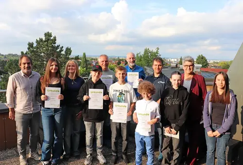 Gruppenfoto mit vier Männern, einer Frau und sieben Kindern und Jugendlichen, die ihre Urkunden und Preis präsentieren.