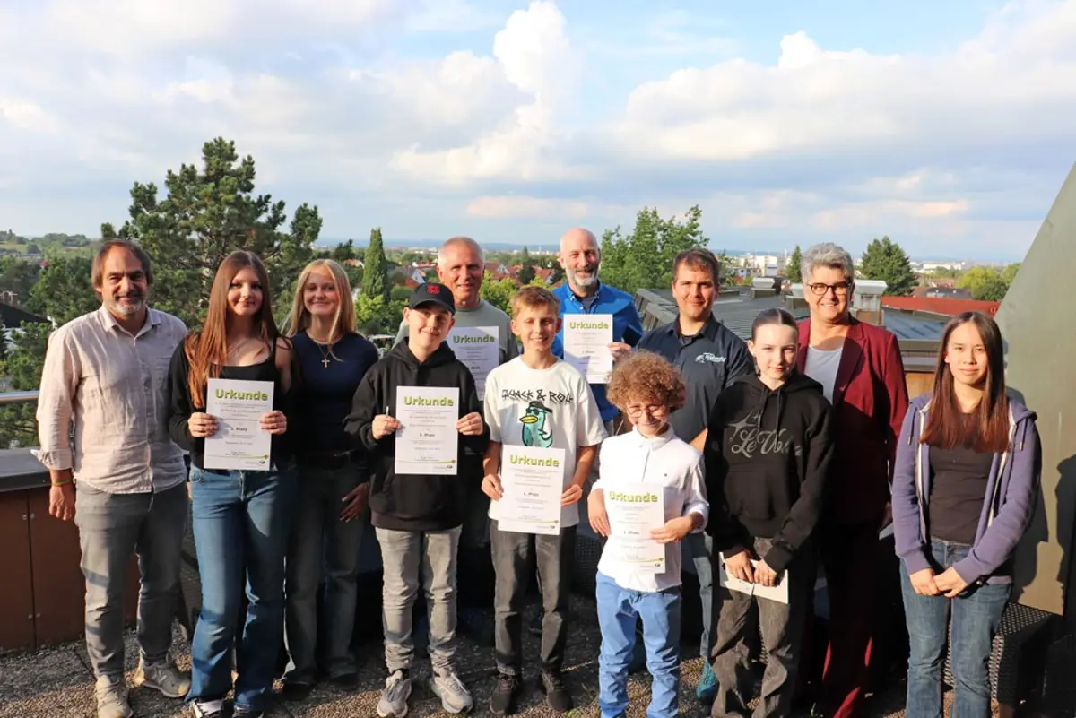 Gruppenfoto mit vier Männern, einer Frau und sieben Kindern und Jugendlichen, die ihre Urkunden und Preis präsentieren.