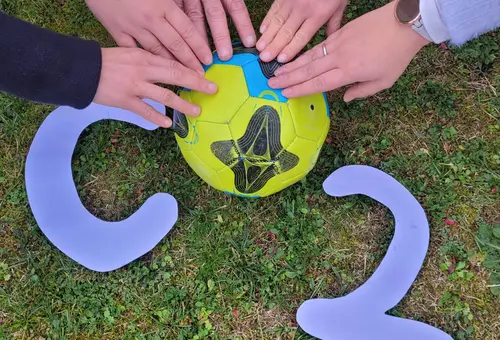 Fünf Hände berühren das Logo CO2. Das O ist durch einen Ball ersetzt, der von der Farbgebung einem Globus ähnelt.