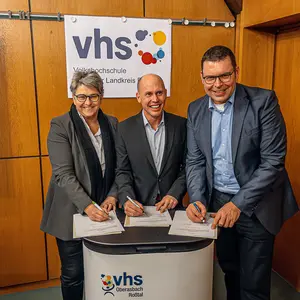 Eine Frau und zwei Männer unterzeichnen jeweils einen Vertrag.