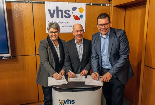 Eine Frau und zwei Männer unterzeichnen jeweils einen Vertrag.