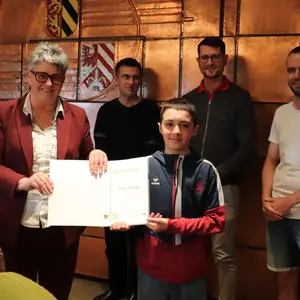 eine Frau und vier Männer vor dem Stadtwappen im Sitzungssaal