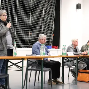 Eine Frau spricht stehend ins Mikrofon und fünf weitere Personen sitzend am Podium.