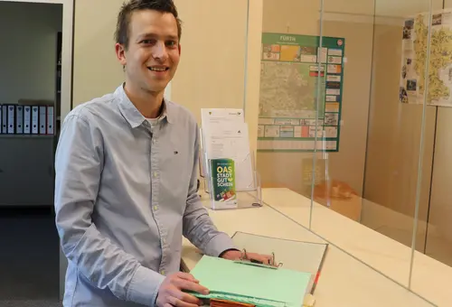 Christian Kuhn steht mit einem Dokumentenordner am Kassentresen. 